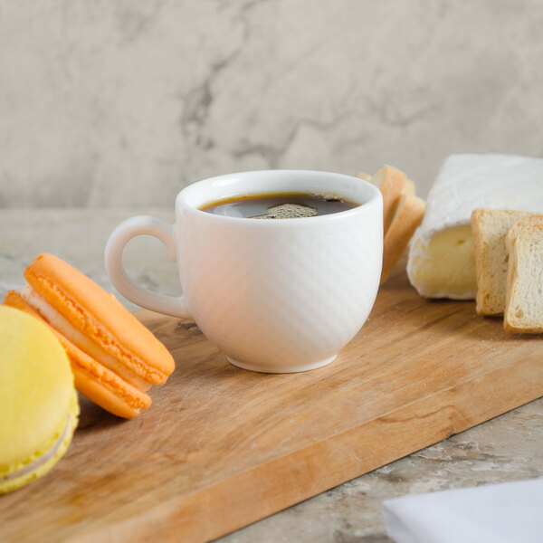 A Villeroy & Boch white porcelain cup of coffee with macarons on a wood surface.