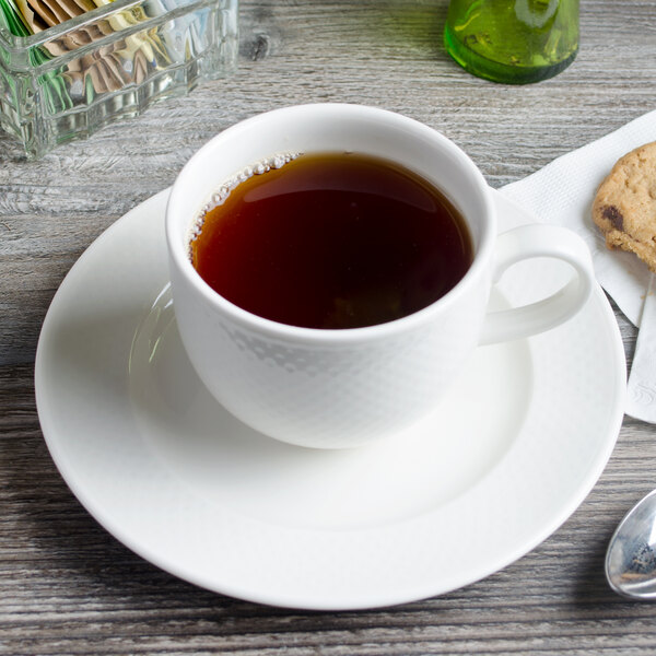 A Villeroy & Boch white porcelain cup of tea on a saucer with a cookie.