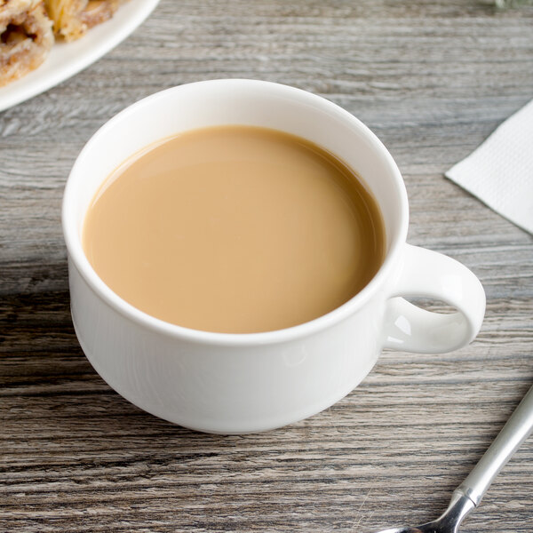 A Villeroy & Boch white porcelain cup of coffee with a spoon on a wood surface.