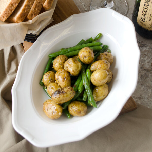 A Villeroy & Boch white porcelain oval deep plate with green beans and potatoes on a table.