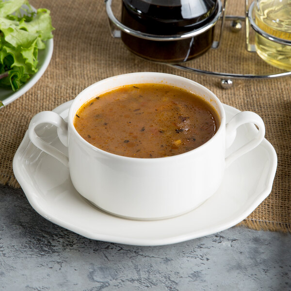 A white porcelain stackable soup cup filled with soup on a plate.