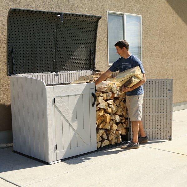 A man loading wood into a brown Lifetime horizontal outdoor shed.