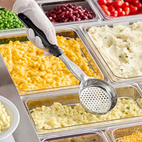 A hand holding a black Vollrath Spoodle over a tray of food.