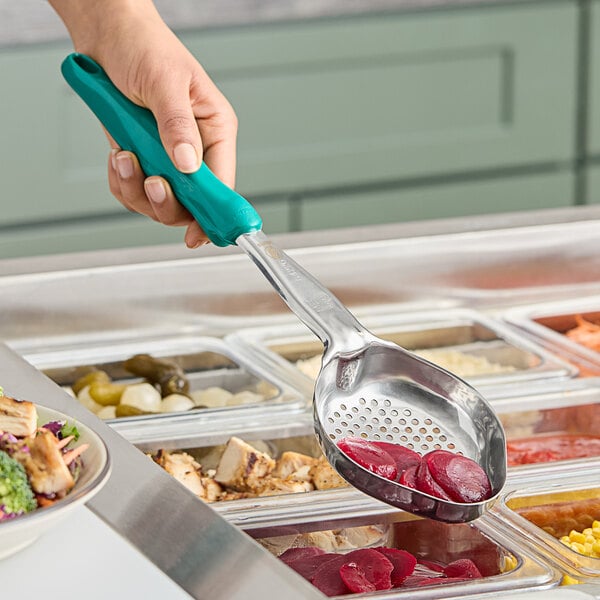 A hand holding a Vollrath teal perforated oval spoodle over a bowl of food.