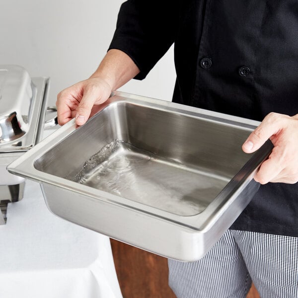 A person holding a stainless steel water pan for a chafer.