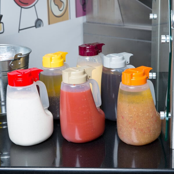 A Tablecraft plastic dispenser jar with a red lid filled with red liquid on a white counter.