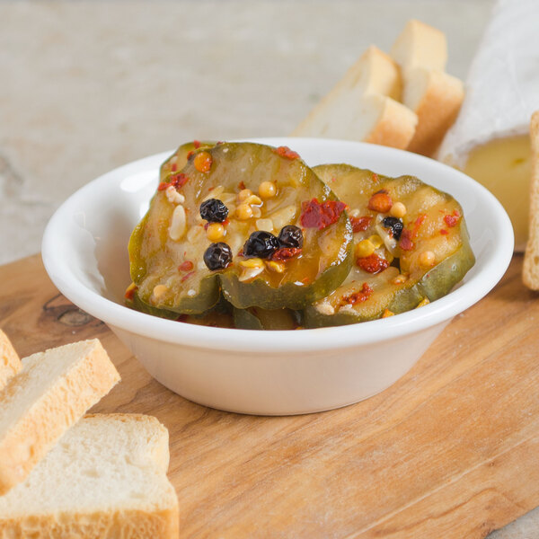 A white Villeroy & Boch porcelain bowl of pickles with bread on a wooden surface.