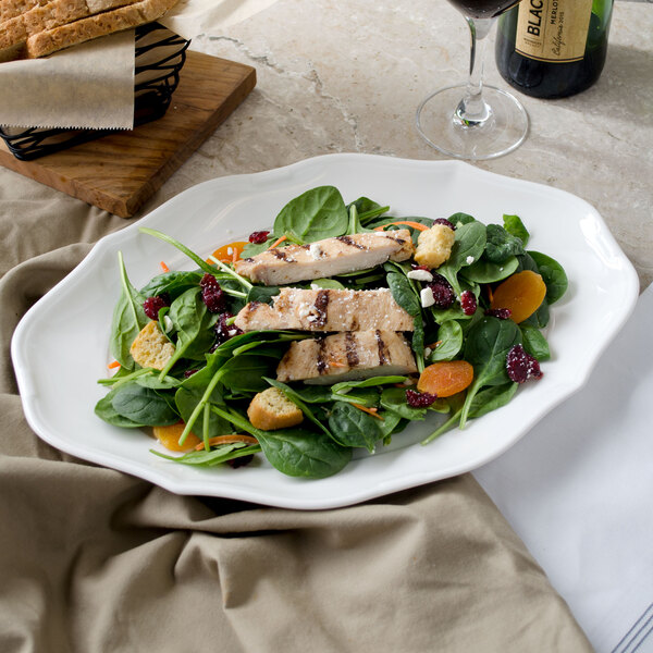 A white porcelain oval plate with salad, chicken, and grapes on it.