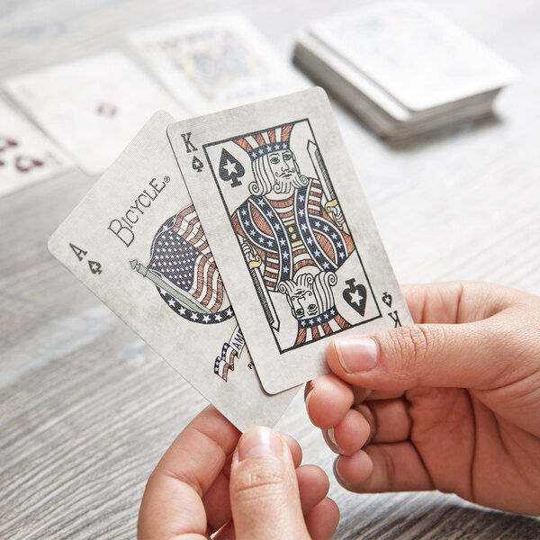 A person holding Bicycle American Flag playing cards on a wooden table.