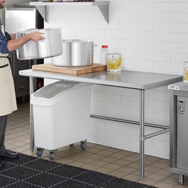 A man in a professional kitchen using a Regency stainless steel work table to hold large pots.