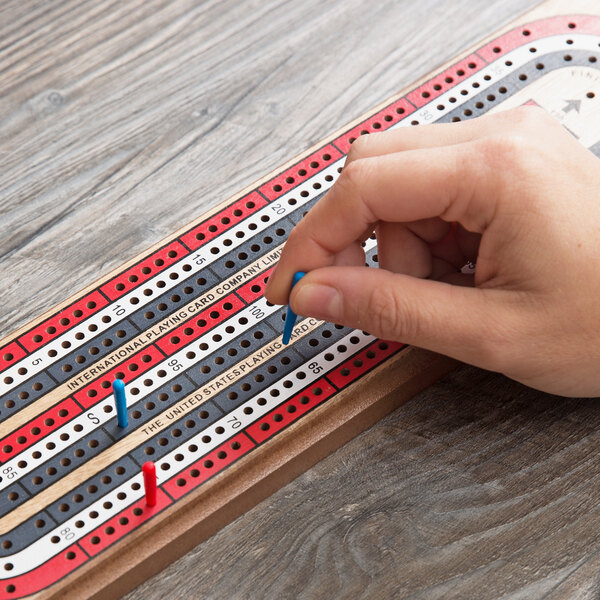 A hand holding a blue tip on a Bicycle 3-Track cribbage board.