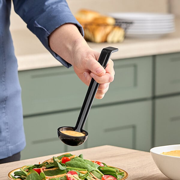 A person using a black Cambro ladle to scoop sauce over a plate of food.