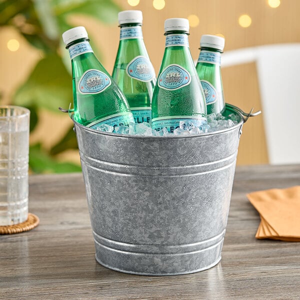 An American Metalcraft galvanized metal bucket filled with soda bottles on a table on an outdoor patio.