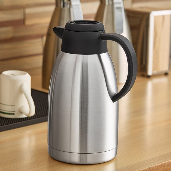 A stainless steel insulated thermal coffee carafe with a black handle and lid.