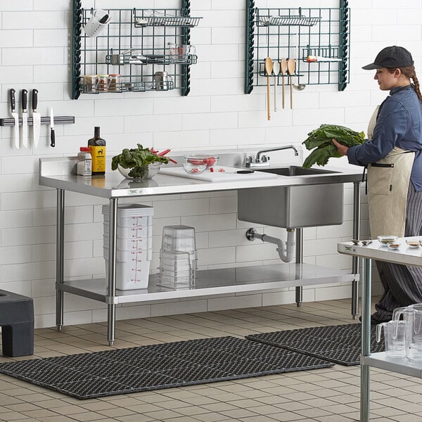 A woman washing vegetables at a Regency stainless steel work table with a sink.