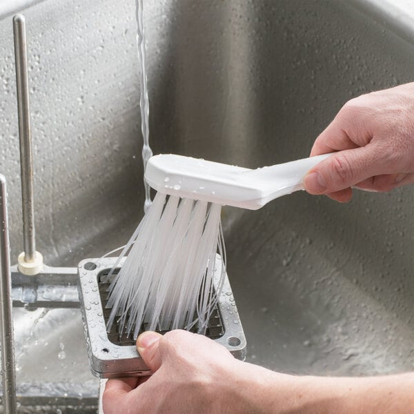 A hand holding a Carlisle Sparta Spectrum white brush with stiff bristles over a sink.