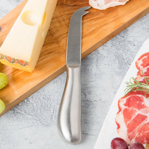 An American Metalcraft stainless steel cheese knife cutting a block of cheese on a wooden surface.