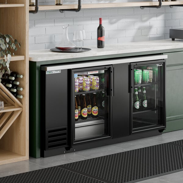 A black glass door back bar refrigerator with LED lighting, stocked with beverages and installed under a countertop.