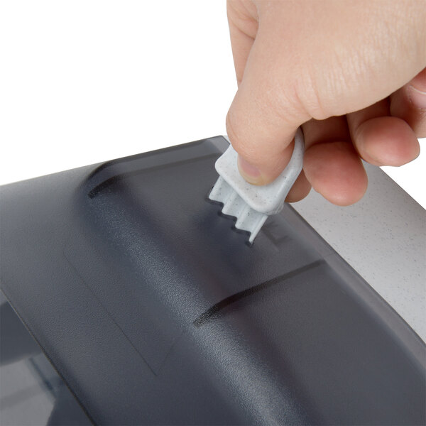 A hand using a white San Jamar R3000TBK toilet tissue dispenser.