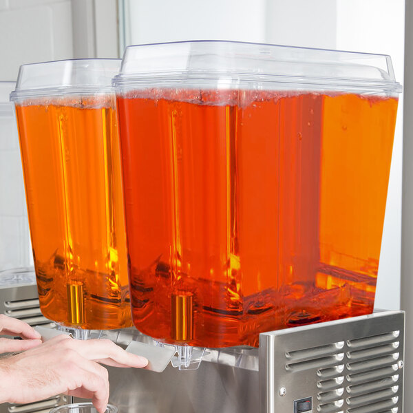 A person using a Crathco refrigerated beverage dispenser to pour orange juice into a glass.