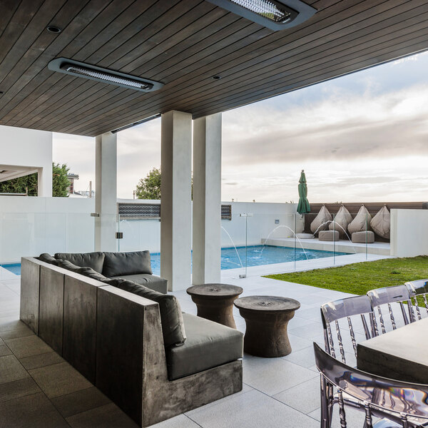 A patio with a Bromic Heating ceiling recess kit above a couch and table near a pool.