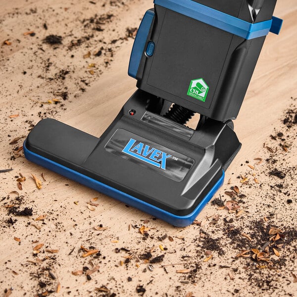 A Lavex 15-inch dual motor upright bagged vacuum cleaner with HEPA filtration being used to clean debris from a hardwood floor.