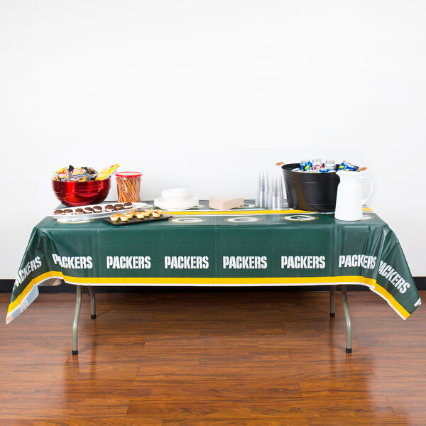 A Green Bay Packers plastic table cover on a table with food.