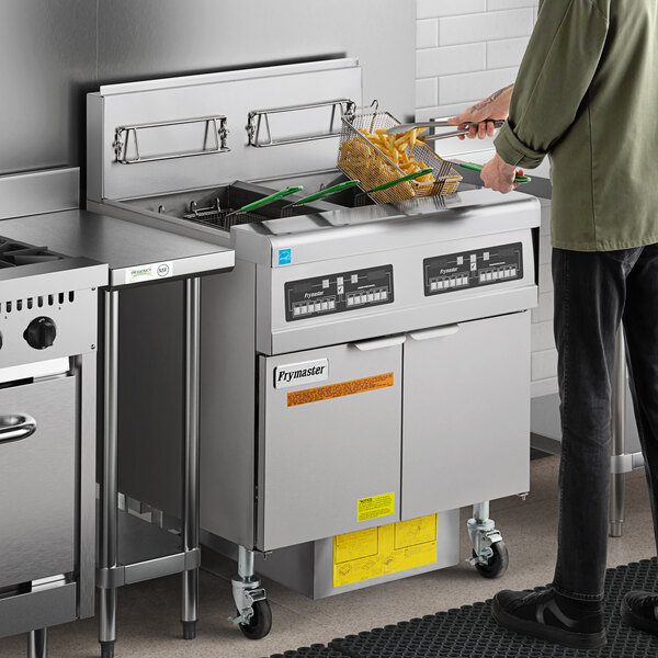 A man cooking food in a commercial kitchen using a Frymaster gas fryer.