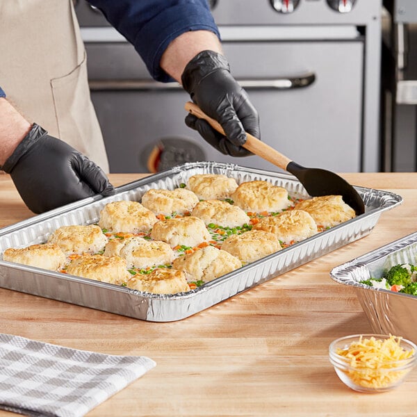 A person in gloves preparing food in a Western Plastics foil steam table pan.