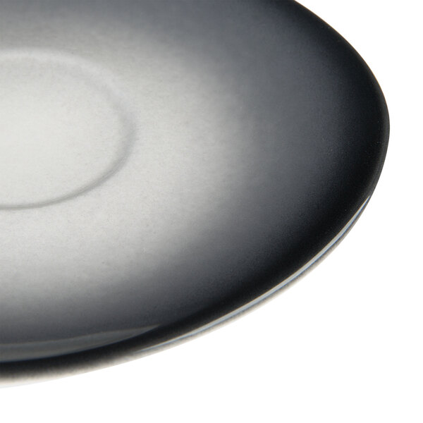 A close-up of a white porcelain saucer with a black pebble design.