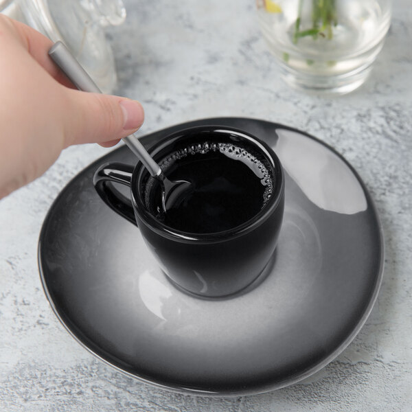 A hand holding a spoon in a black porcelain saucer.