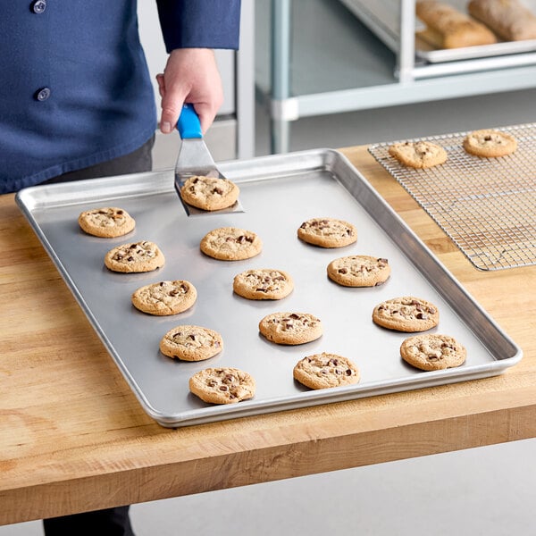 A person using a Chicago Metallic wire in rim aluminum sheet pan to cut cookies.