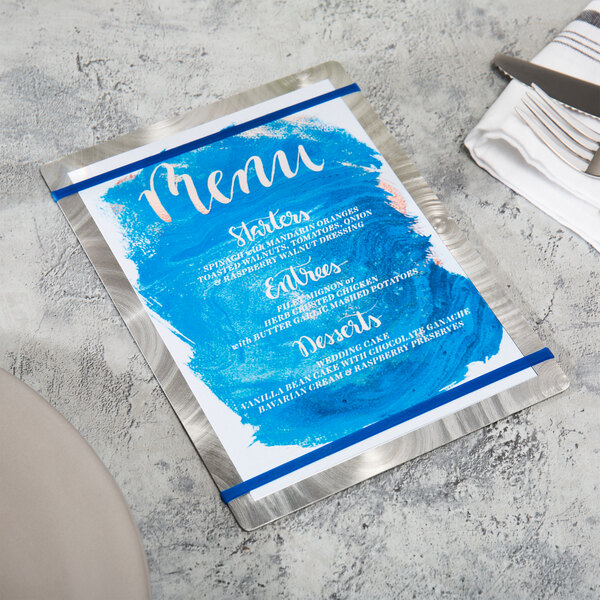 A navy blue Alumitique menu board with silver swirls and navy bands on a table with silverware.