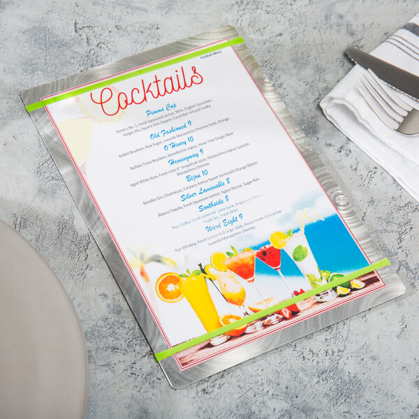 A Menu Solutions Alumitique menu board with green bands on a table with a white plate, a knife, and a fork.