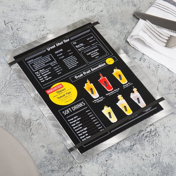 A Menu Solutions Alumitique aluminum menu board with black bands on a table with a knife and fork.