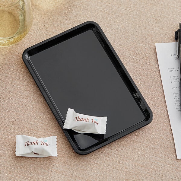 A black Carlisle standard tip tray with a white packet and a pen on it.