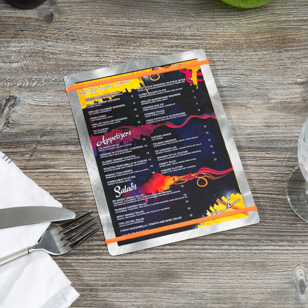An Alumitique customizable aluminum menu board with orange bands on a table with a plate, fork, and knife.