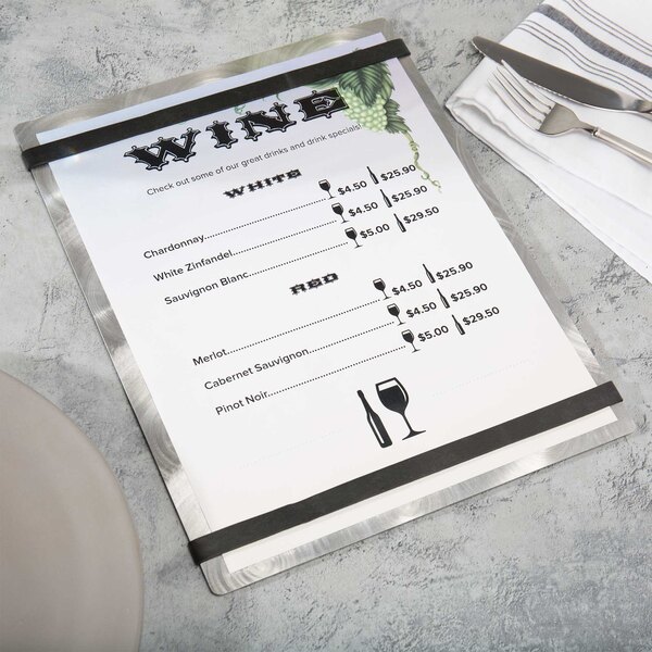 An Alumitique swirl aluminum menu board with black bands on a table with silverware and a napkin.