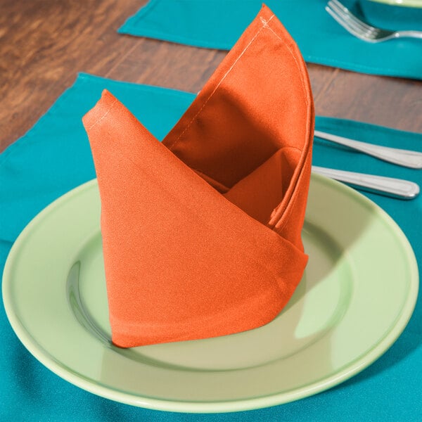 An orange Intedge cloth napkin folded on a green plate.