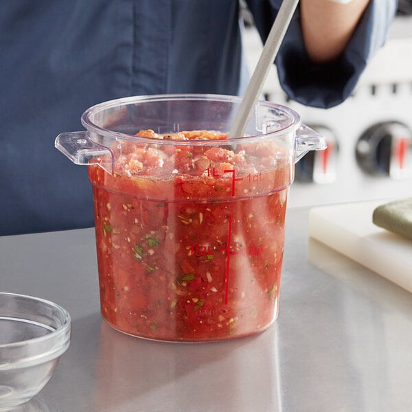 A person stirring red sauce in a Choice clear plastic container.