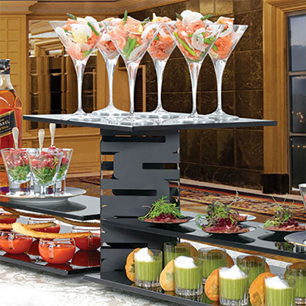 A buffet table with a couple of Rosseto black matte multi-level risers holding different drinks and appetizers.