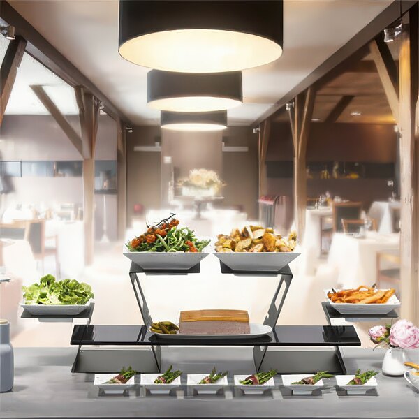 A Rosseto black matte display riser with two square porcelain bowls of food on a buffet table.