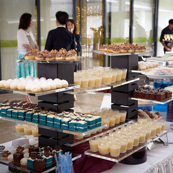 A Rosseto black matte steel multi-level riser with a walnut base displaying desserts on a table.