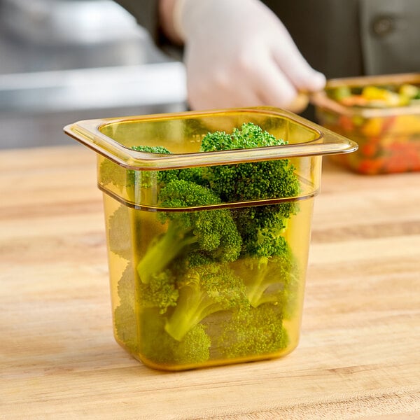 A person cutting broccoli in a Cambro plastic food pan on a counter.