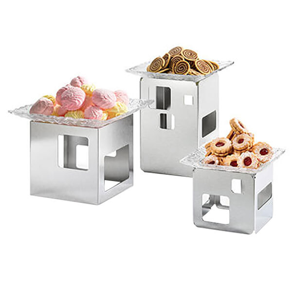 A Rosseto stainless steel display riser with three metal trays of desserts on it.
