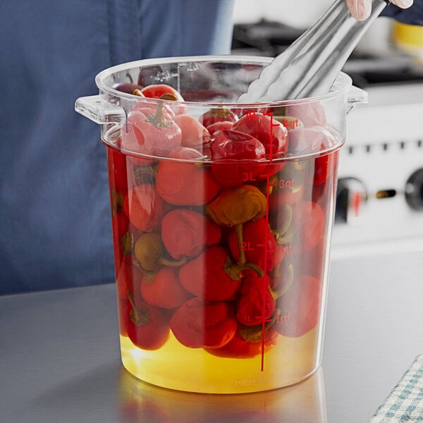 A person stirring a large clear round container of red tomatoes with a spoon.