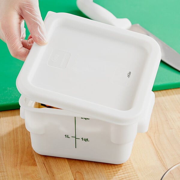 A gloved hand closing a white square polypropylene food storage container lid.