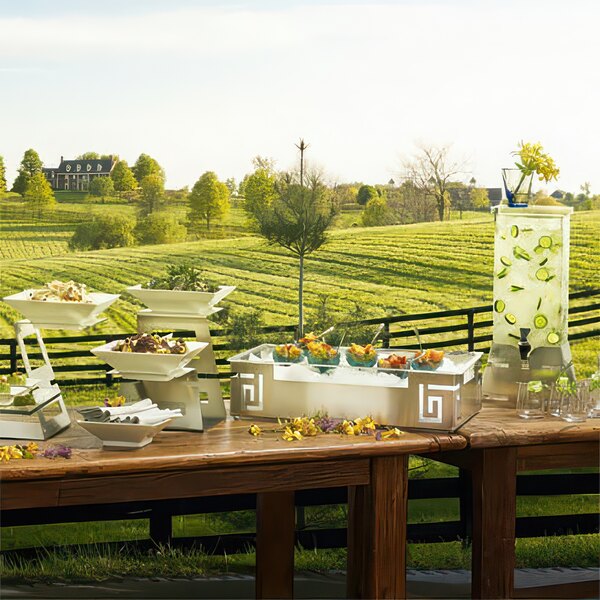 A Rosseto stainless steel pyramid riser on a buffet table with food on it.