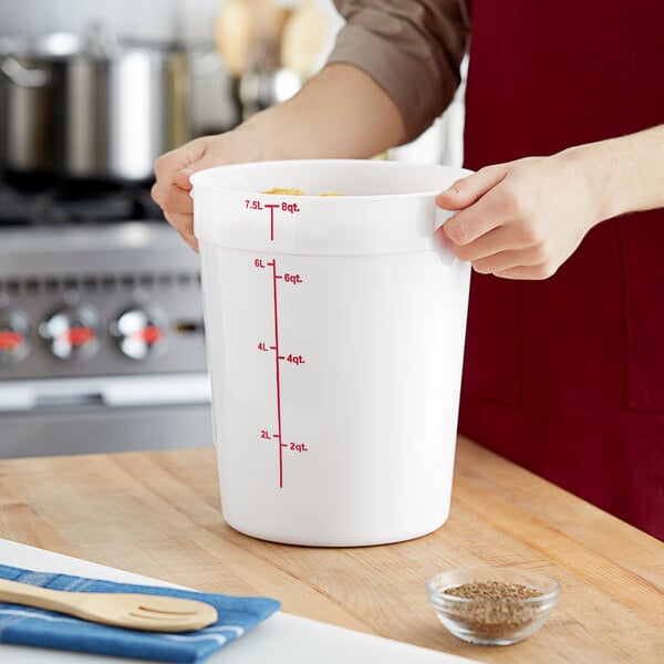 A person pouring brown grain into a large white Choice food storage container with a measuring cup.