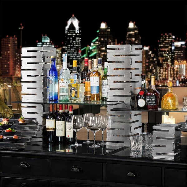 A Rosseto stainless steel riser on a table with a variety of bottles and glasses.